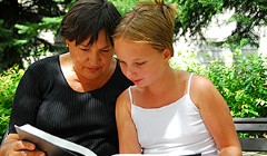 Kvinna och flicka läser bok i park