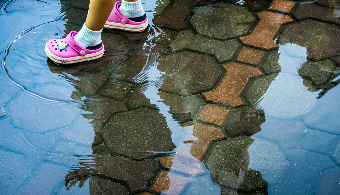 Barnfot med rosa sko i vatten på gata