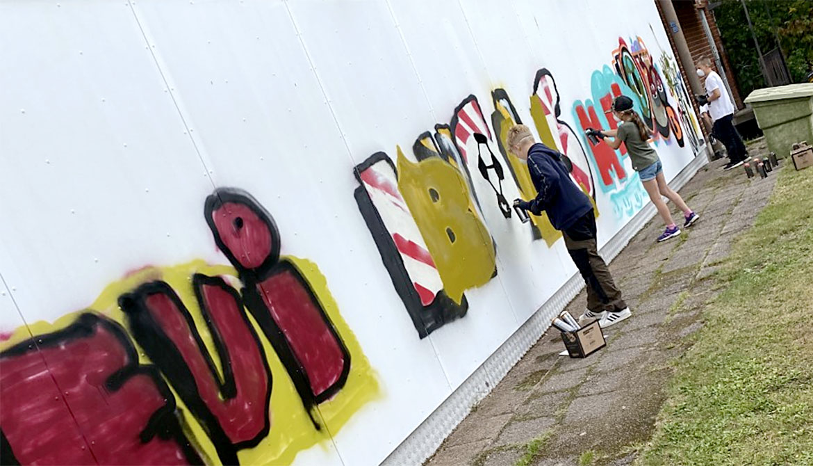 Flera ungdomar målar grafitti på vit vägg.