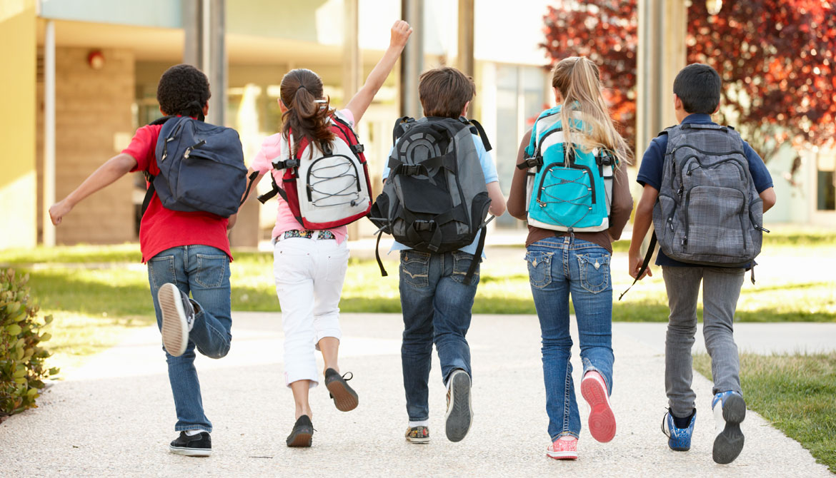 Skolelever springer in i skolan med ryggsäckar på ryggen.