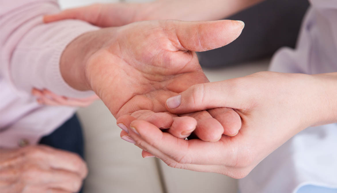 En person håller i en äldre persons hand.