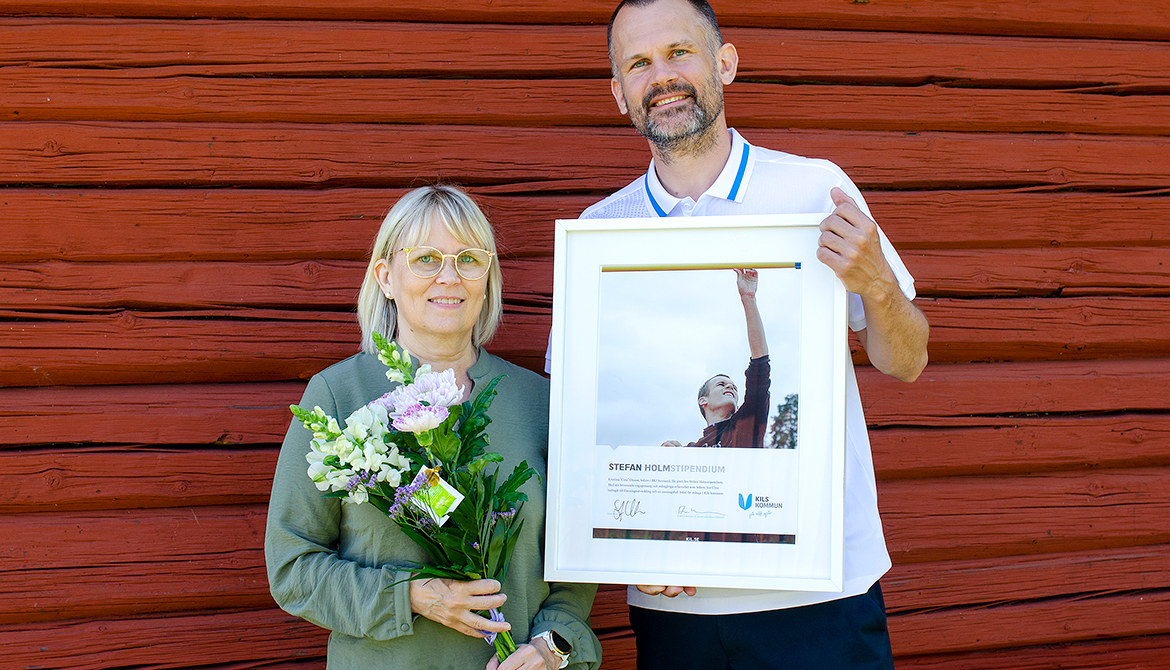 Kristina ”Cina” Olsson med blommor i handen och Stefan Holm till höger med diplom. De står framför en faluröd vägg.