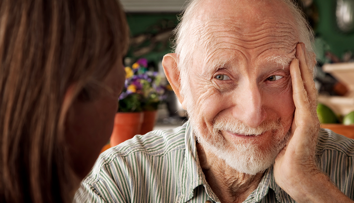 Fotografi av äldre leende man med grått helskägg. 